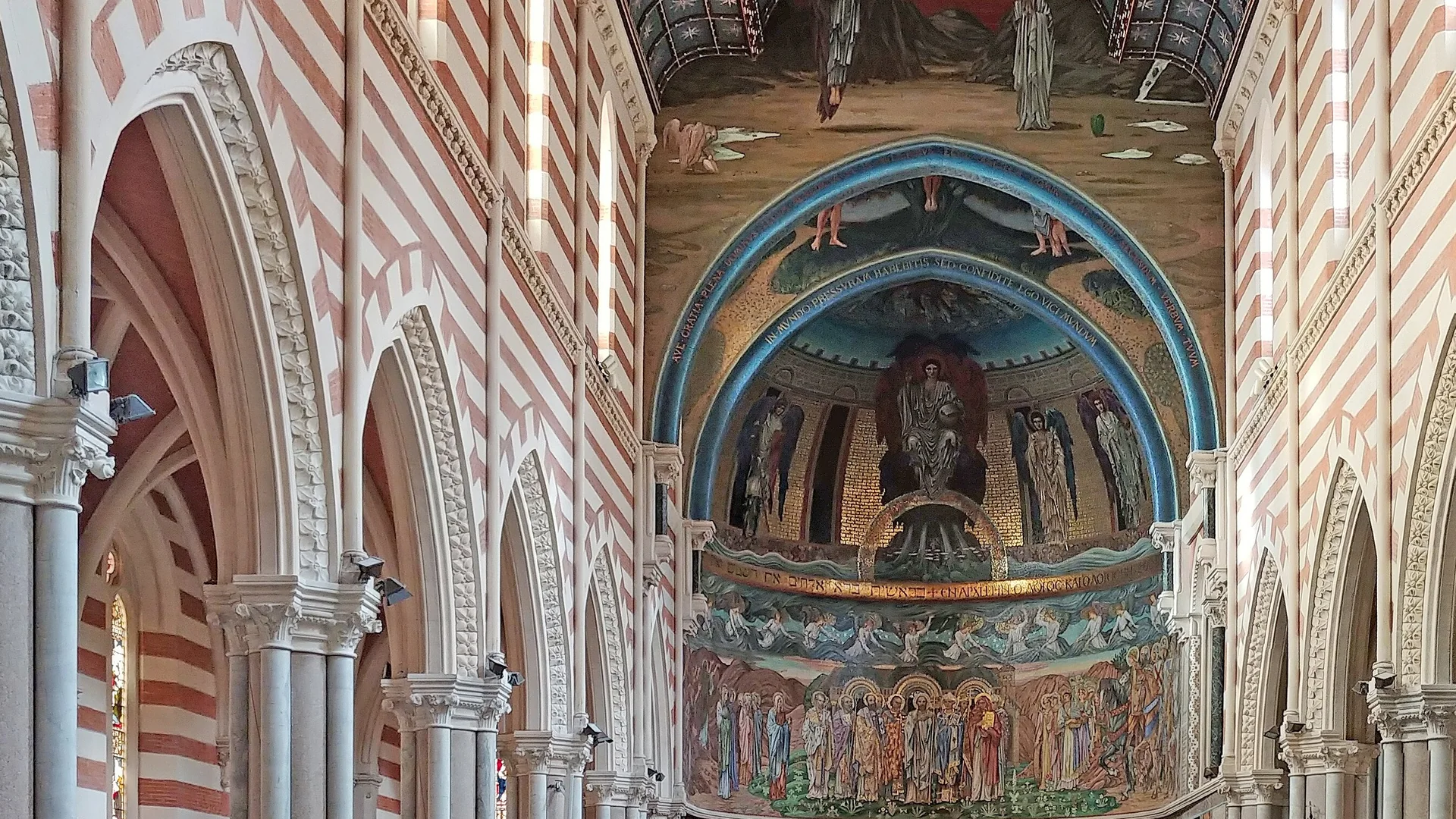 Looking down a Rome church nave banded in red and cream, under a blue ceiling scattered with stars, to an apse glowing with gold mosaics.